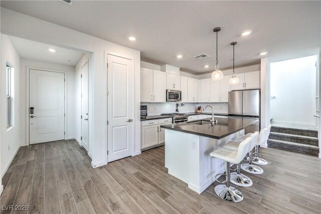 kitchen featuring dark countertops, appliances with stainless steel finishes, a sink, light wood-style floors, and a breakfast bar