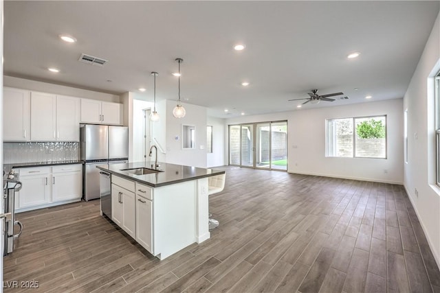 kitchen featuring visible vents, dark countertops, dark wood-type flooring, a sink, and stainless steel appliances