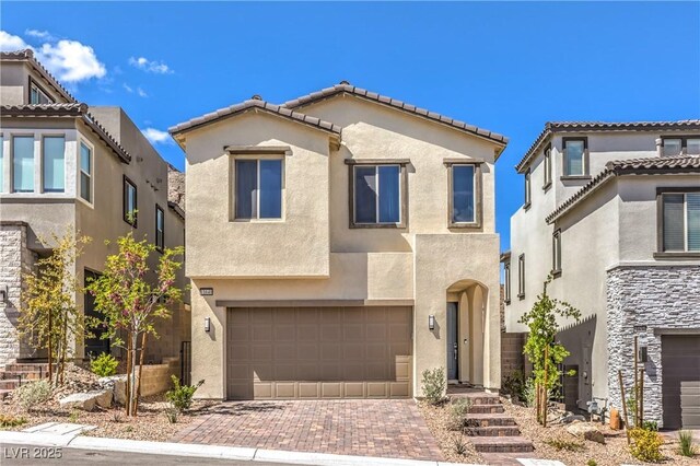 mediterranean / spanish-style home featuring stucco siding, an attached garage, and decorative driveway