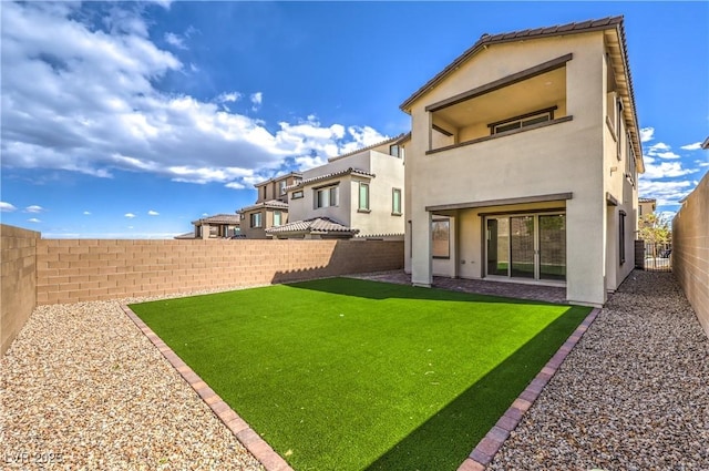 rear view of property featuring a yard, a balcony, a fenced backyard, and stucco siding