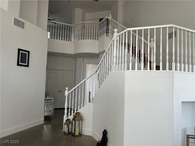staircase with ceiling fan, visible vents, a towering ceiling, and baseboards