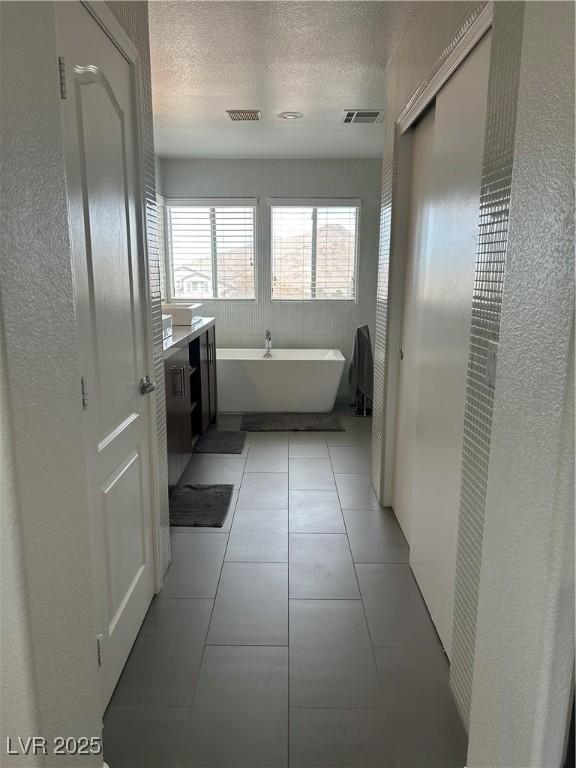 bathroom featuring a textured ceiling, a soaking tub, tile patterned flooring, and visible vents