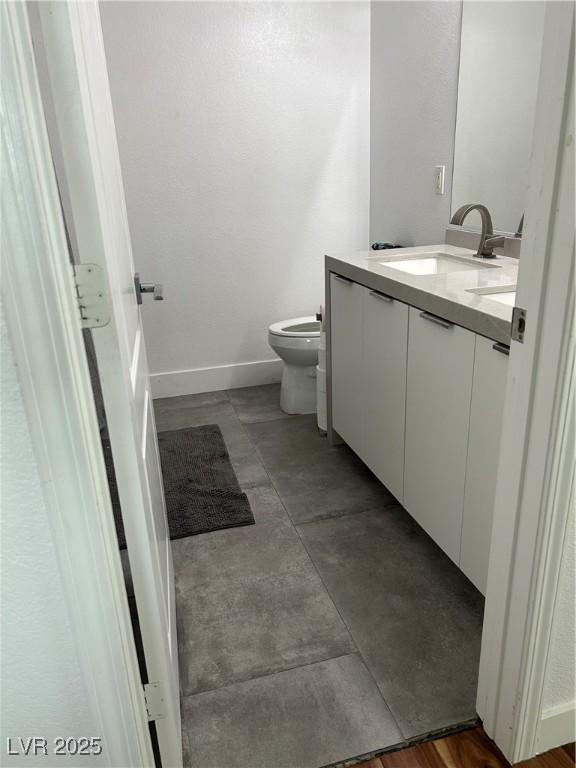 bathroom featuring a sink, toilet, double vanity, and baseboards