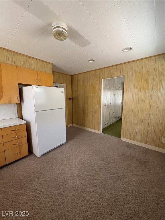 kitchen with baseboards, light countertops, freestanding refrigerator, wooden walls, and carpet floors