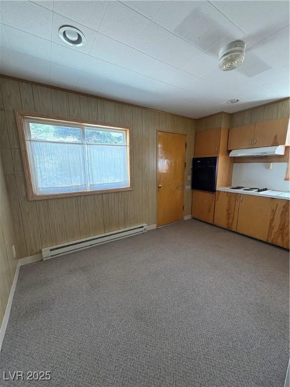 unfurnished living room with wooden walls, a baseboard heating unit, light colored carpet, and a healthy amount of sunlight