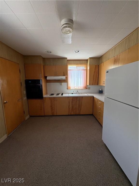 kitchen with white appliances, light countertops, under cabinet range hood, light colored carpet, and a sink