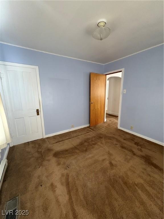 unfurnished room featuring carpet floors, baseboards, arched walkways, and visible vents