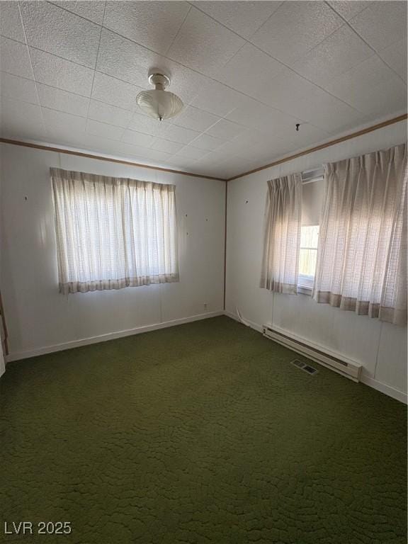 empty room featuring plenty of natural light, a baseboard heating unit, dark carpet, and crown molding