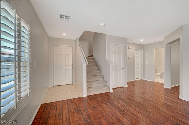 foyer entrance featuring hardwood / wood-style floors, baseboards, visible vents, and stairs