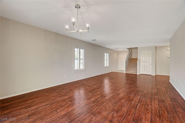 unfurnished living room with baseboards, an inviting chandelier, stairs, visible vents, and wood finished floors