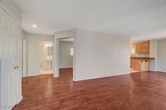 unfurnished living room with dark wood-type flooring, a sink, baseboards, and recessed lighting