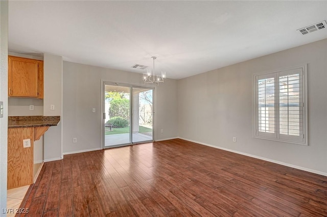 unfurnished dining area featuring a chandelier, wood finished floors, baseboards, and visible vents