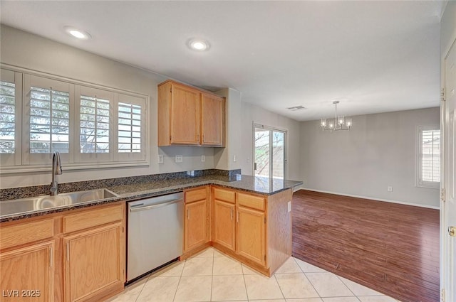 kitchen featuring stainless steel dishwasher, a peninsula, a sink, light wood finished floors, and a notable chandelier