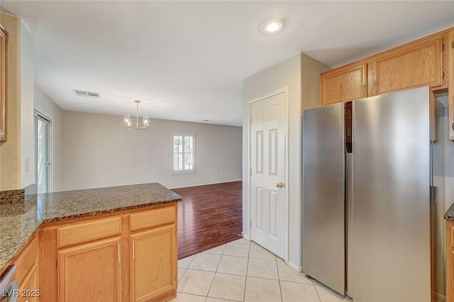 kitchen featuring visible vents, light tile patterned floors, freestanding refrigerator, a peninsula, and dark stone counters
