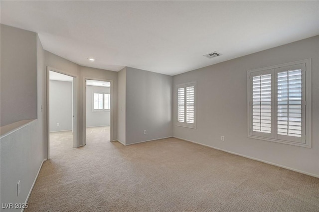 empty room featuring light colored carpet, baseboards, visible vents, and a wealth of natural light