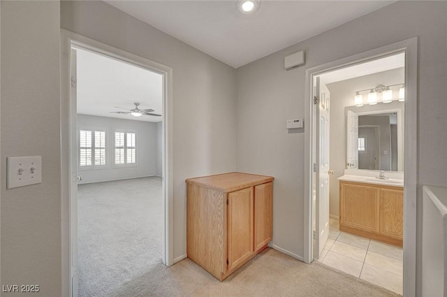 hallway featuring light tile patterned flooring, light colored carpet, a sink, and baseboards