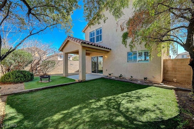rear view of property featuring stucco siding, a fire pit, a fenced backyard, a tile roof, and a yard