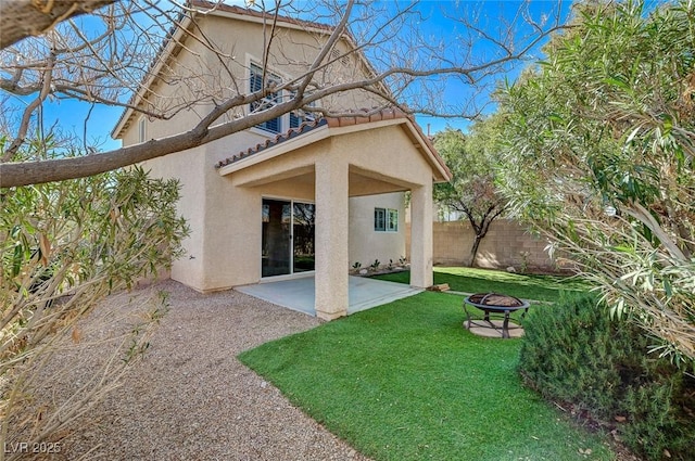 rear view of house with a fire pit, a tiled roof, a yard, fence, and stucco siding