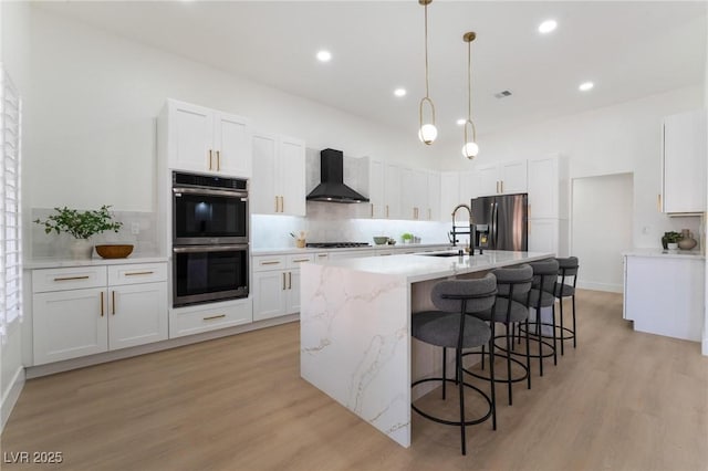 kitchen with double oven, gas stovetop, refrigerator with ice dispenser, wall chimney range hood, and a sink