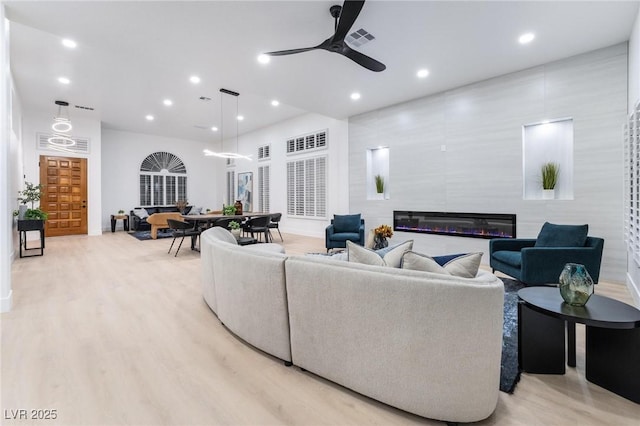 living area with a glass covered fireplace, baseboards, recessed lighting, a ceiling fan, and visible vents