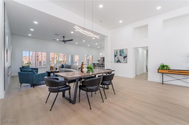 dining room with light wood-style flooring, a towering ceiling, baseboards, and recessed lighting