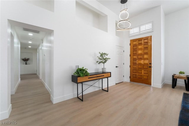 foyer entrance with light wood-type flooring, a towering ceiling, and baseboards