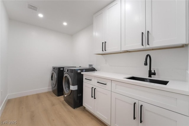 washroom featuring a sink, light wood-style flooring, visible vents, cabinet space, and washing machine and clothes dryer
