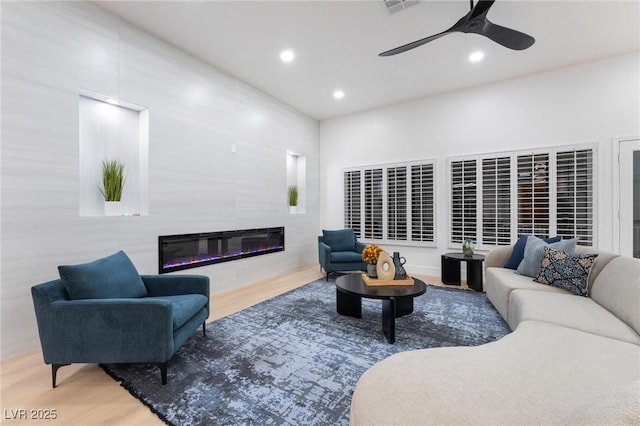living room with wood finished floors, ceiling fan, a glass covered fireplace, and recessed lighting