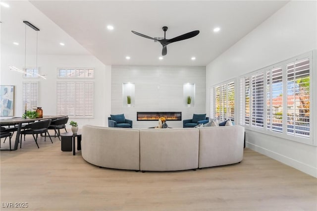 living room with a glass covered fireplace, a wealth of natural light, light wood-type flooring, and ceiling fan