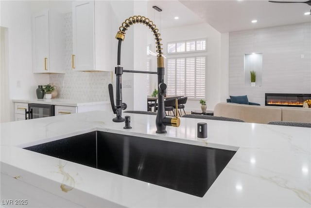 kitchen featuring a fireplace, light stone countertops, white cabinets, a sink, and backsplash