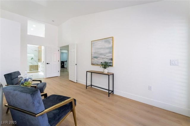 sitting room featuring light wood-style floors, high vaulted ceiling, and baseboards