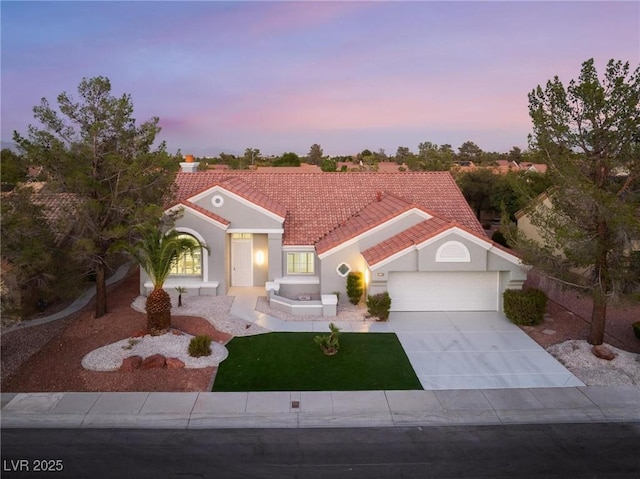 mediterranean / spanish home with a tiled roof, stucco siding, a front yard, an attached garage, and driveway