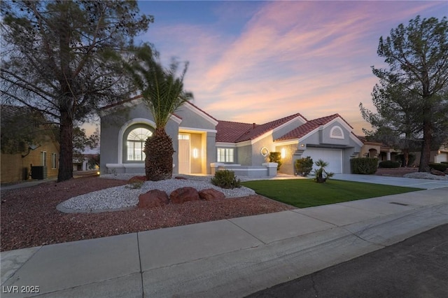view of front of property featuring stucco siding, driveway, an attached garage, a tile roof, and a lawn