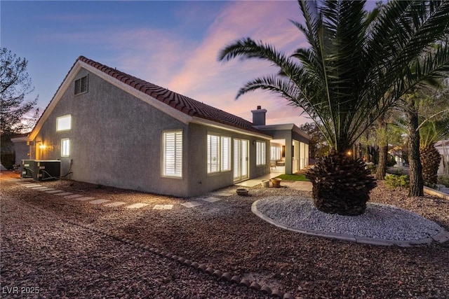 property exterior at dusk featuring stucco siding, cooling unit, and a tile roof