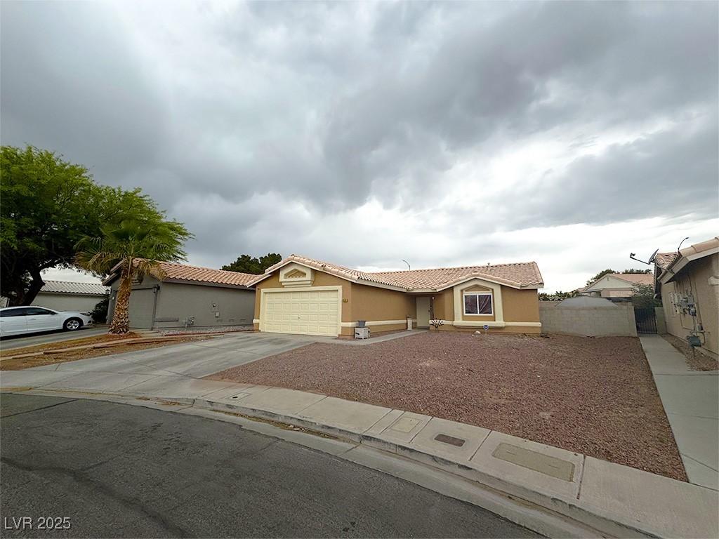 view of front of property featuring fence, stucco siding, a tiled roof, an attached garage, and driveway