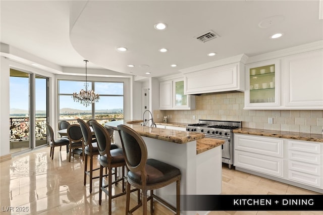 kitchen featuring visible vents, light stone counters, premium range hood, high end stainless steel range oven, and backsplash