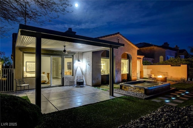 back of house at night featuring a patio, stucco siding, fence, and a ceiling fan