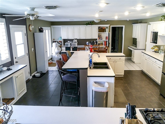 kitchen featuring a sink, dark tile patterned floors, an island with sink, and visible vents