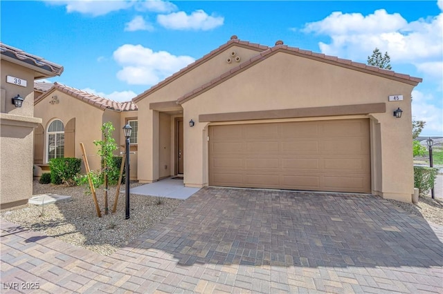view of front of home featuring a garage, stucco siding, a tiled roof, and decorative driveway