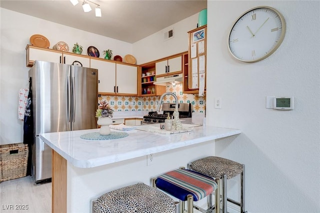 kitchen with under cabinet range hood, open shelves, a peninsula, decorative backsplash, and appliances with stainless steel finishes