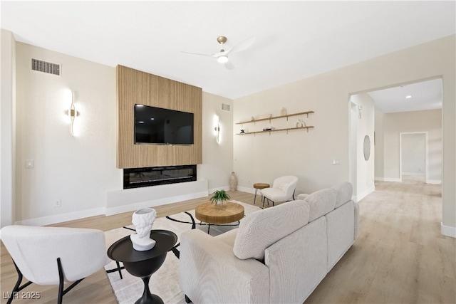 living room featuring baseboards, light wood finished floors, visible vents, and a large fireplace