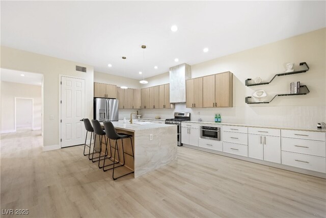kitchen with light wood finished floors, a sink, visible vents, appliances with stainless steel finishes, and premium range hood