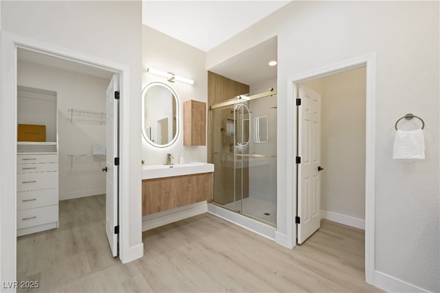 bathroom with wood finished floors, a walk in closet, baseboards, a shower stall, and vanity