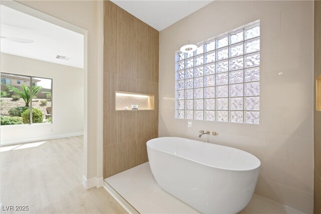 full bathroom with a soaking tub, visible vents, and wood finished floors