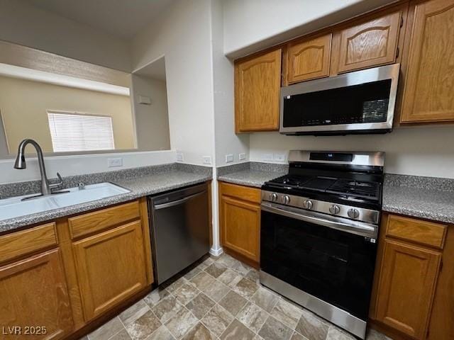 kitchen featuring a sink, brown cabinetry, appliances with stainless steel finishes, and stone finish floor