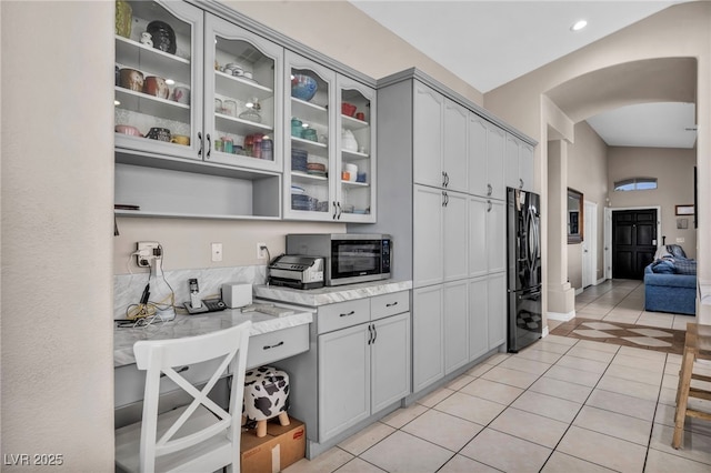 90 Ancient Hills Ln, Henderson, NV 89074 - kitchen featuring stainless steel microwave, black fridge with ice dispenser, arched walkways, light tile patterned flooring, and glass insert cabinets