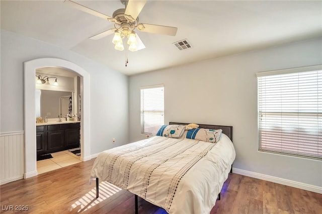 9383 Borough Park St, Las Vegas, NV 89178 - bedroom featuring light wood-type flooring, arched walkways, ensuite bath, visible vents, and baseboards