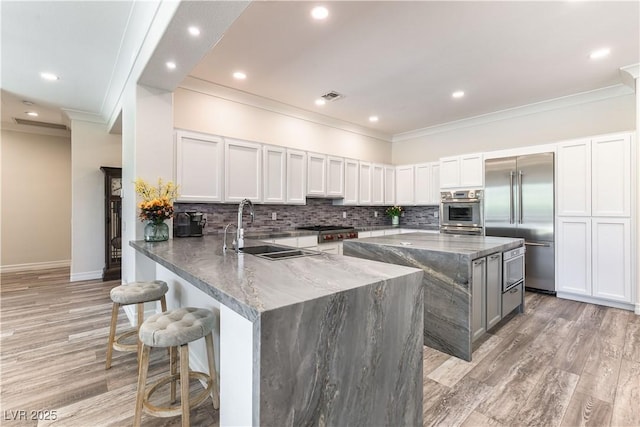 kitchen featuring stainless steel appliances, a kitchen bar, dark stone countertops, visible vents, and backsplash