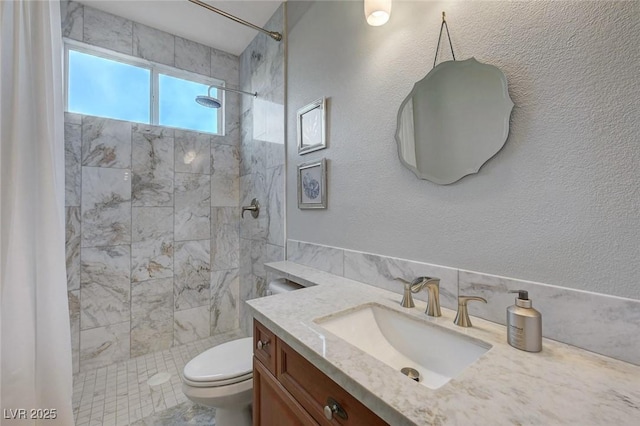 bathroom featuring toilet, tiled shower, and vanity