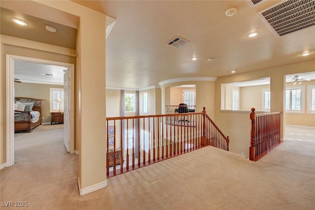 hallway with an upstairs landing, ornamental molding, visible vents, and carpet floors